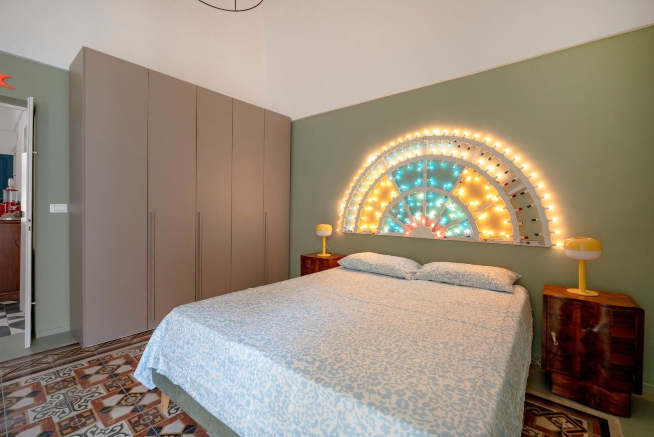 Een slaapkamer met een bed, een kledingkast, een nachtkastje en een wandlamp.