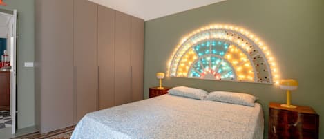 A bedroom with a bed, a wardrobe, a nightstand, and a wall-mounted light fixture.
