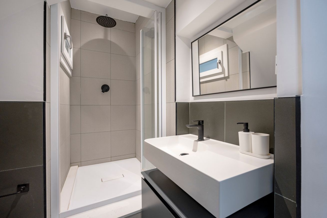 A modern bathroom with a large white sink, two mirrors, and a shower area.