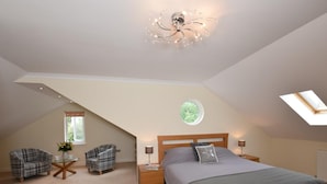 Ein Schlafzimmer mit schrägen Wänden, einem Oberlicht, einem Bett mit Holz Kopfteil, zwei Stühlen, einem kleinen Tisch und einem flauschigen Teppich.