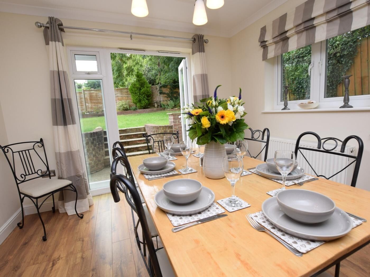 Un coin repas avec une table dressée pour quatre personnes, un vase de fleurs et une vue sur le jardin, visible à travers la porte vitrée.