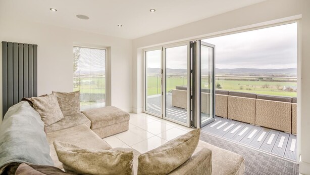 Een moderne woonkamer met een hoekbank en een schuifdeur naar een balkon met uitzicht op het landschap.