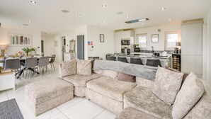 Een moderne woonkamer met een modulaire bank, eethoek, keuken en een groot raam.