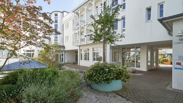 A white building with balconies, a garden area with plants, and a clear sky. - Ferienwohnung mit Ahoi-rabatt in Sellin (Sellin)