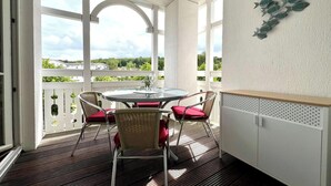 A balcony with a glass table and chairs, white railings, and a view of greenery. - Ferienwohnung in Sellin (Sellin)