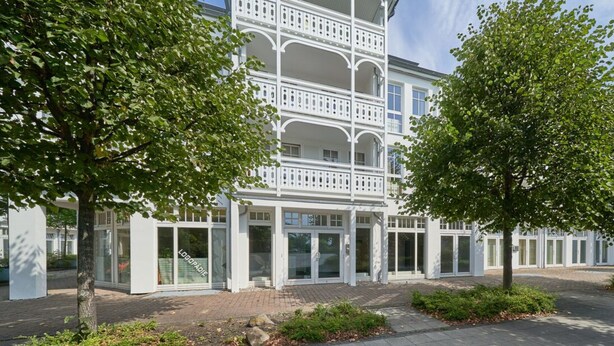 A modern building with a white facade, multiple balconies, and a paved entrance area with greenery. - Ferienwohnung in Sellin (Sellin)
