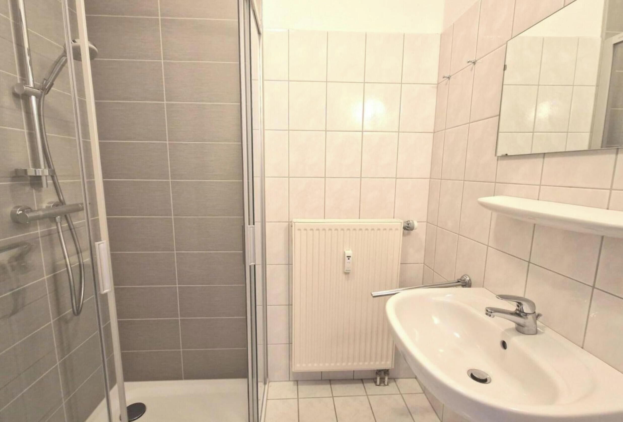 Et badeværelse med bruser, håndvask og spejl.