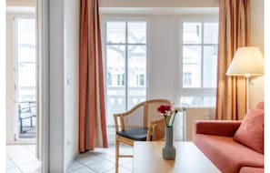 Et værelse med sofa, stol, bord, lampe og et vindue med gardiner.