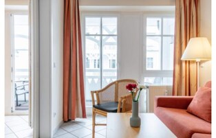 Una habitación con sofá, silla, mesa, lámpara y ventana con cortinas.