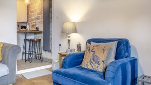 A living room with a blue sofa, a lamp, and a kitchen area with stools. - 1 Bed in Crich (oc-h37533) (Crich)