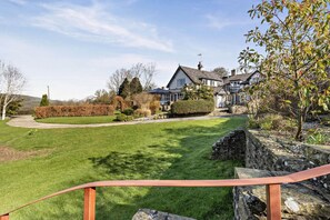 A residential property with a well-maintained lawn, stone wall, and a house with multiple windows and a chimney.