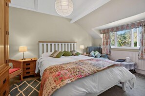 A bedroom with a bed, a chair, a nightstand, a lamp, and a window with curtains.