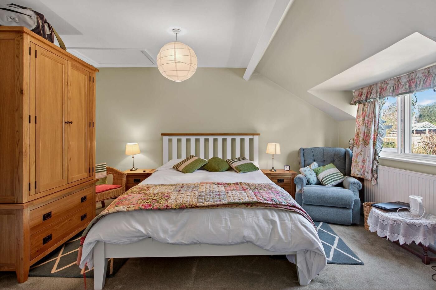 Een slaapkamer met een bed, een kledingkast, een stoel, een lamp en een raam.