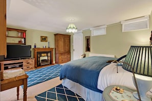 Un dormitorio con una cama, televisión, chimenea, lámpara y una mesita con un plato.