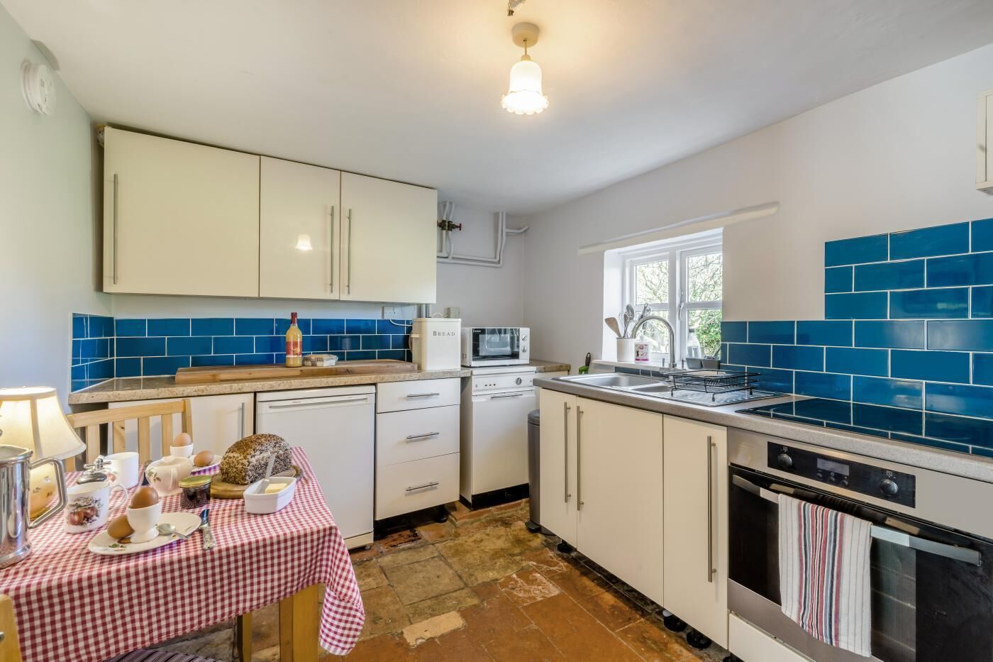 Een keuken met witte kasten, een magnetron, een spoelbak en een raam.