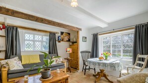 Una sala acogedora con un sofá, una mesa de madera, una mesa de comedor con sillas y una ventana con cortinas.