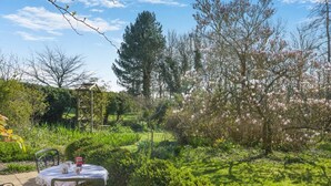 Un jardín con mesa y sillas, rodeado de follaje y árboles florecientes.
