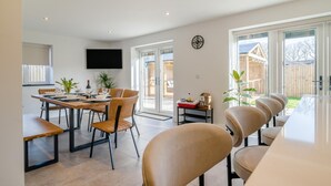 Un espace repas moderne avec une longue table, des chaises et un téléviseur fixé au mur.