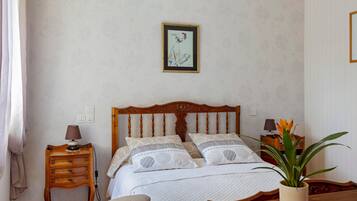 Een slaapkamer met een houten bed, nachtkastjes, een lamp, een potplant en een lijst aan de muur.