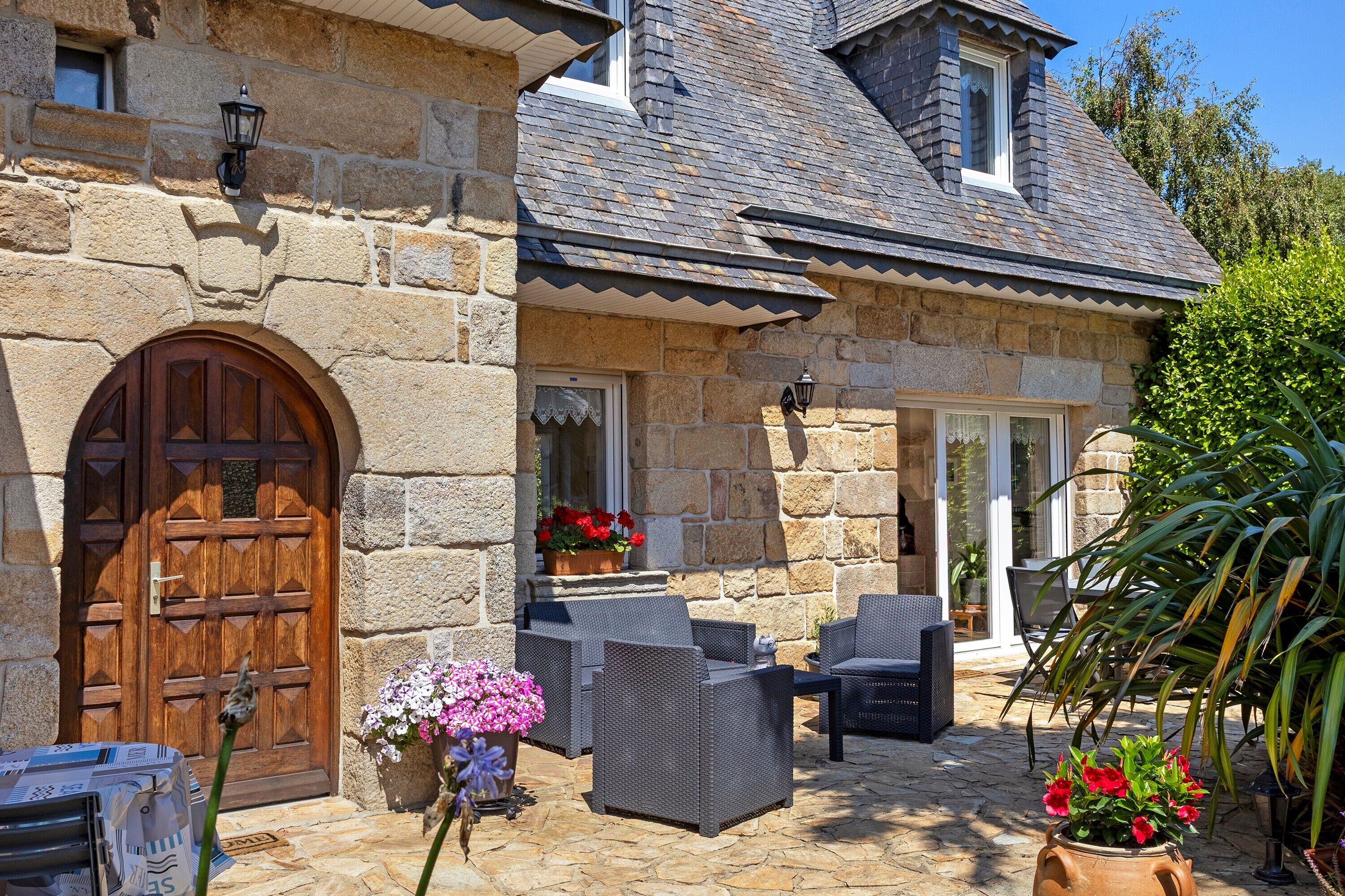 A stone building with a large wooden door, outdoor seating, and potted flowers.