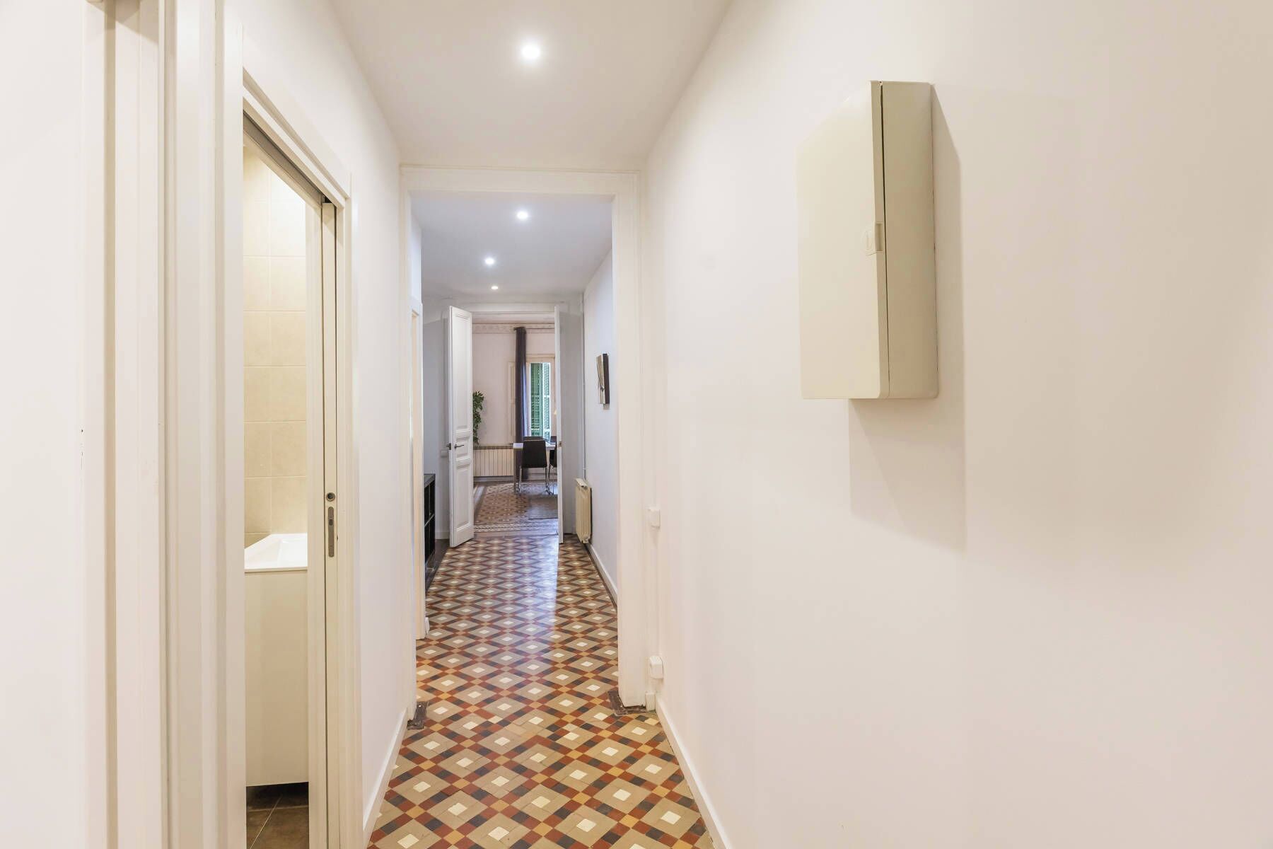 A hallway with patterned flooring, white walls, and a door on the left.