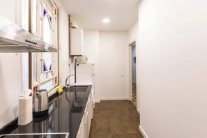 A narrow kitchen with a black countertop, a stainless steel range hood, a built-in oven, and a window with a blue view. - 31agrvc1136  lovely flat in the city centre (Barcelona)