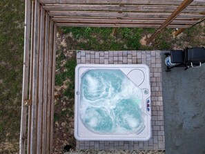 Ein Whirlpool mit einer hölzernen Pergola darüber, einer Ziegelterrasse und einem tragbaren Grill.