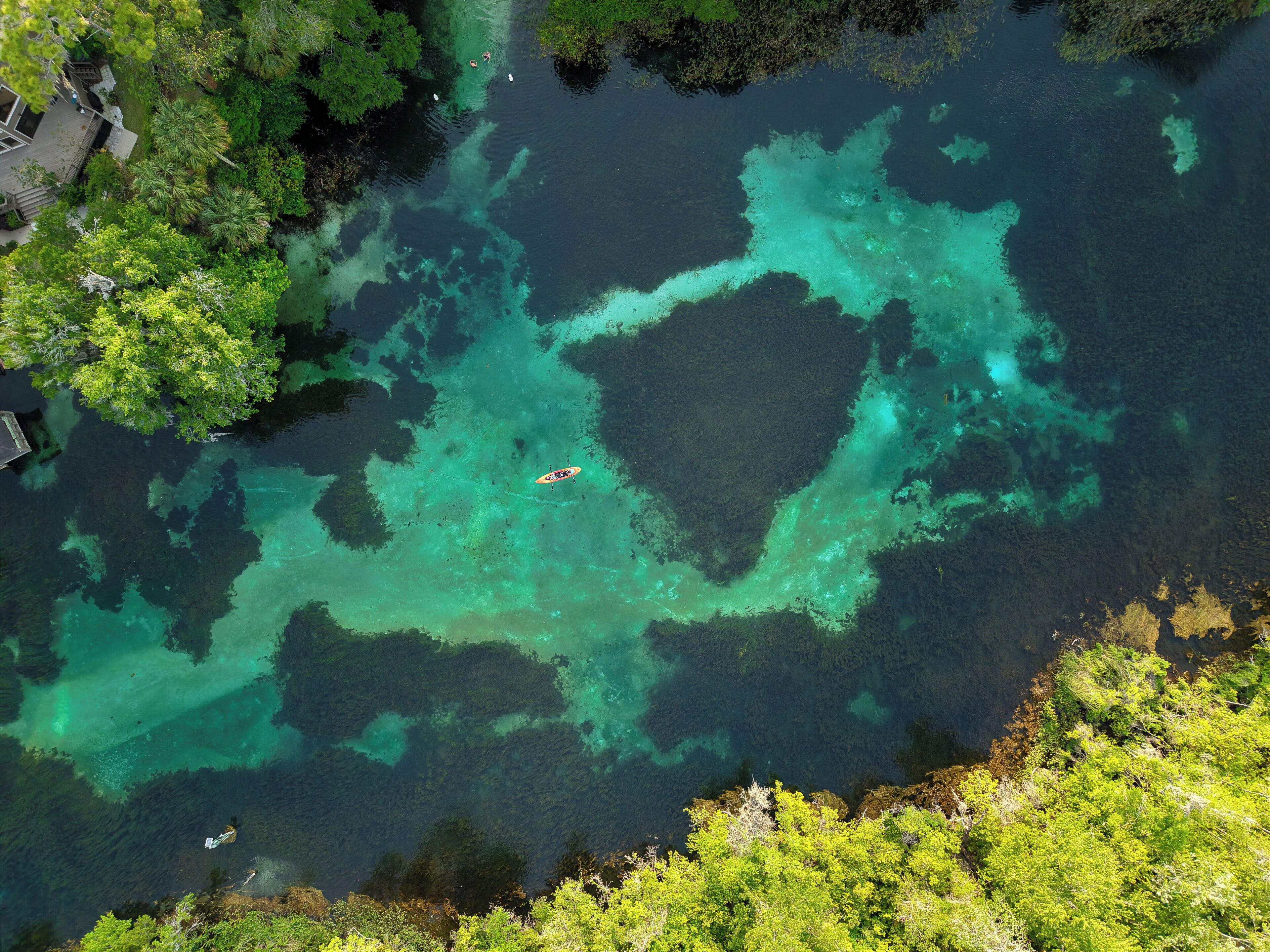 An aerial view of a clear, turquoise body of water surrounded by dense greenery.