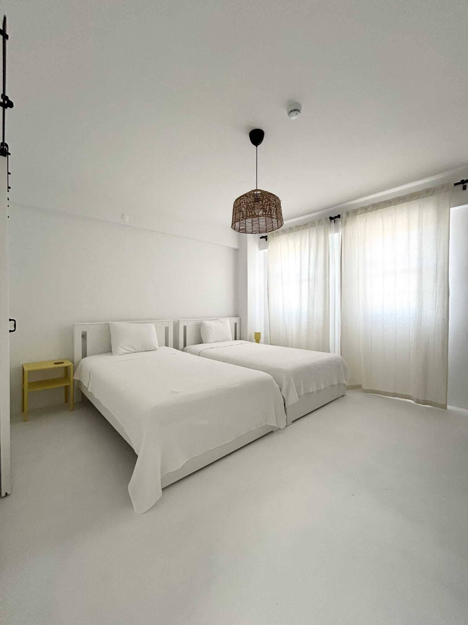 Un dormitorio minimalista con dos camas, una mesita de noche pequeña y una lámpara colgante.