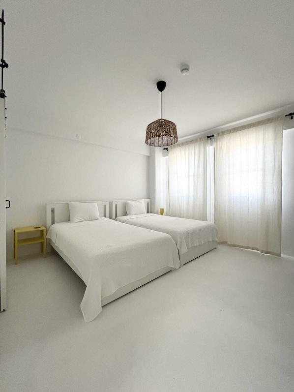 Un dormitorio minimalista con dos camas, una mesita de noche pequeña y una lámpara colgante.