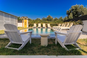 Un área junto a la piscina con sillas Adirondack blancas, una mesita y una puerta amarilla al fondo.
