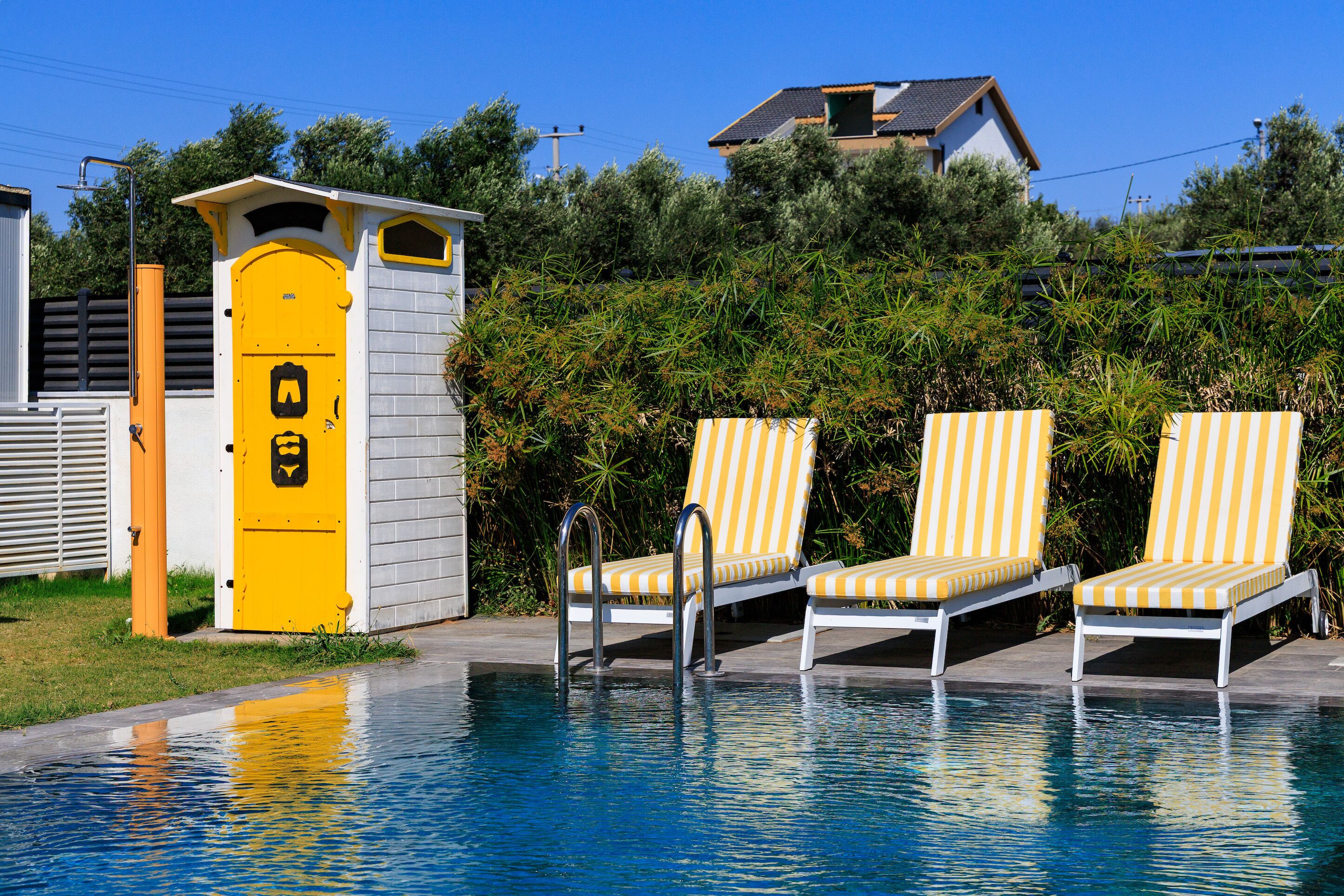 Una piscina con sillas de descanso y un pequeño edificio con una puerta amarilla.