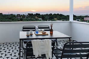 A balcony with a table set for two, chairs, a vase with dried flowers, and a tray with a cup and water bottles.