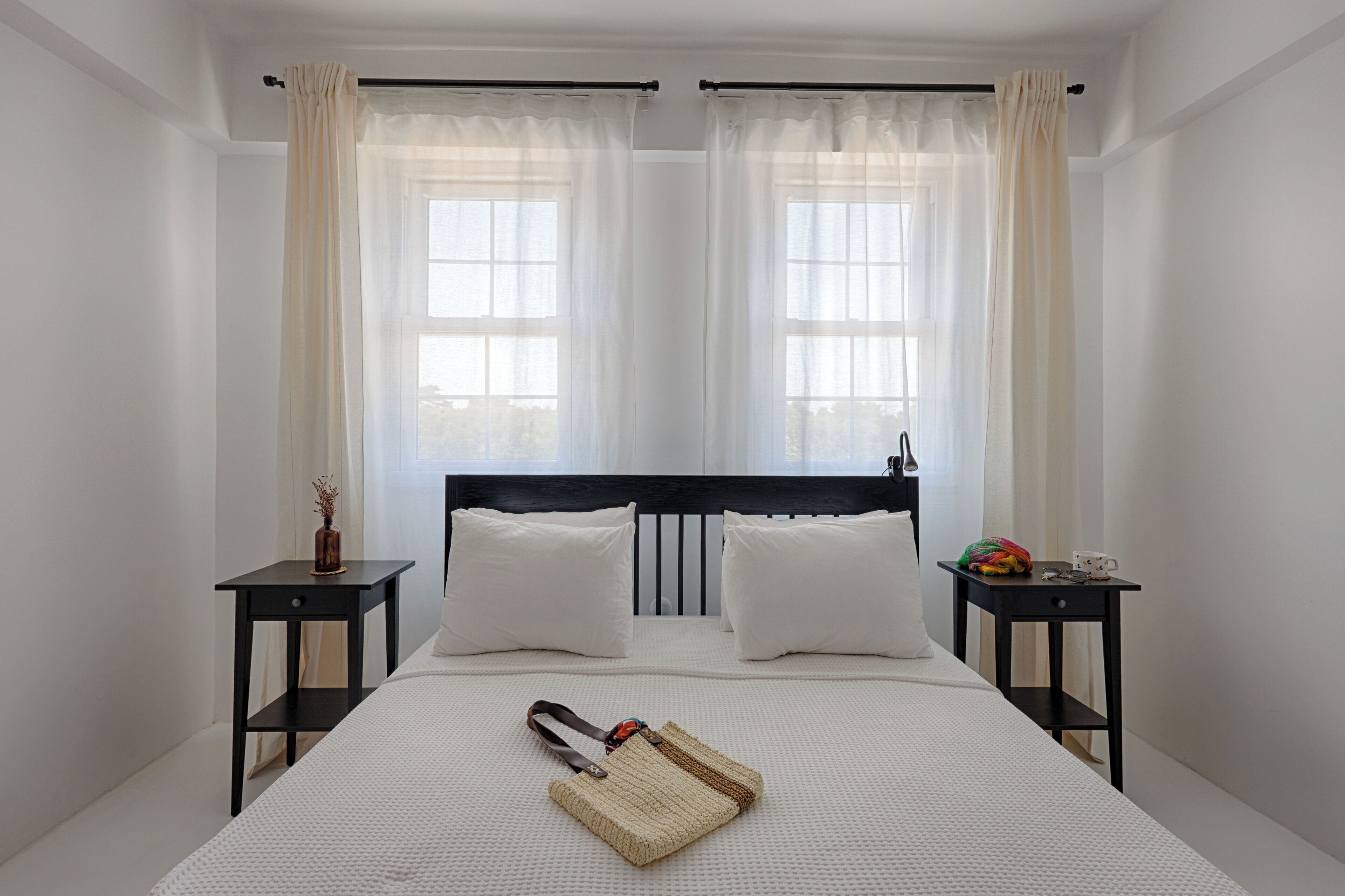 Un dormitorio con una cama, dos mesitas de noche, cabecero y una ventana con cortinas.