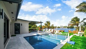 En swimmingpool med et net, omgivet af en patio med liggestole og udsigt til vandet.