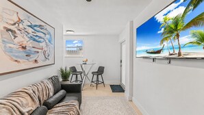 En moderne stue med en sofa, et lille bord med stole, et billede og et stort fjernsyn der viser et strandmotiv.