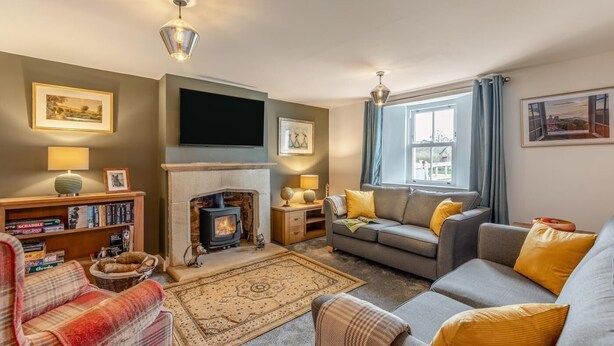 A cozy living room with a fireplace, a sofa, a bookshelf, and a flat-screen TV. - 2 Bed in Caldbeck (oc-b38644) (Caldbeck)