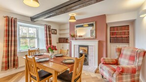 A dining room with a wooden table set for four, a fireplace, a bookshelf, and a plaid armchair. - 2 Bed in Caldbeck (oc-b38644) (Caldbeck)
