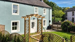 A light blue cottage with white trim, a wooden gate, and a well-maintained garden. - 2 Bed in Caldbeck (oc-b38644) (Caldbeck)