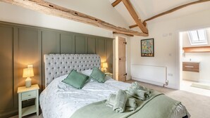 A bedroom with a tufted headboard, a bed with green pillows, a nightstand with a lamp, a radiator, and a window with a view. - 2 Bed in Caldbeck (oc-b38644) (Caldbeck)