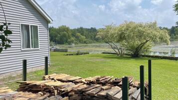 A house with a yard, a stack of firewood, and a tree with white blossoms.