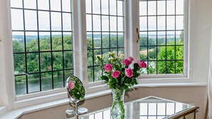 Ein Zimmer mit großem Fenster, einem Spiegel und einer Vase mit Blumen.