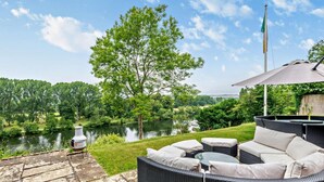 Eine Terrasse mit Korbmöbeln, einem Steinweg und Blick auf einen See.
