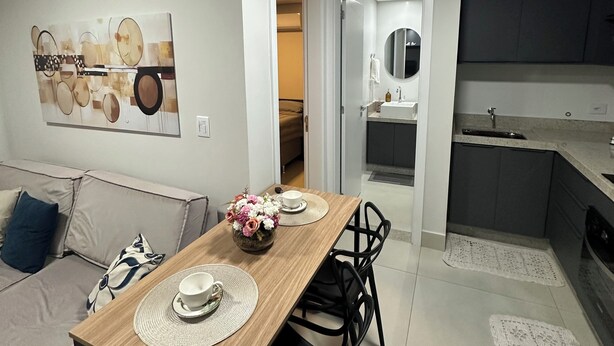 Un salon moderne avec une table à manger en bois, des chaises noires, un canapé et un coin cuisine doté de meubles gris.