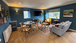 Een woonkamer met een eettafel, stoelen, een bank, een radiator, een televisie en een raam met uitzicht.