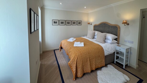 Een slaapkamer met een bed, nachtkastjes, wandlampen, een vloerkleed en ingelijste foto's aan de muur.