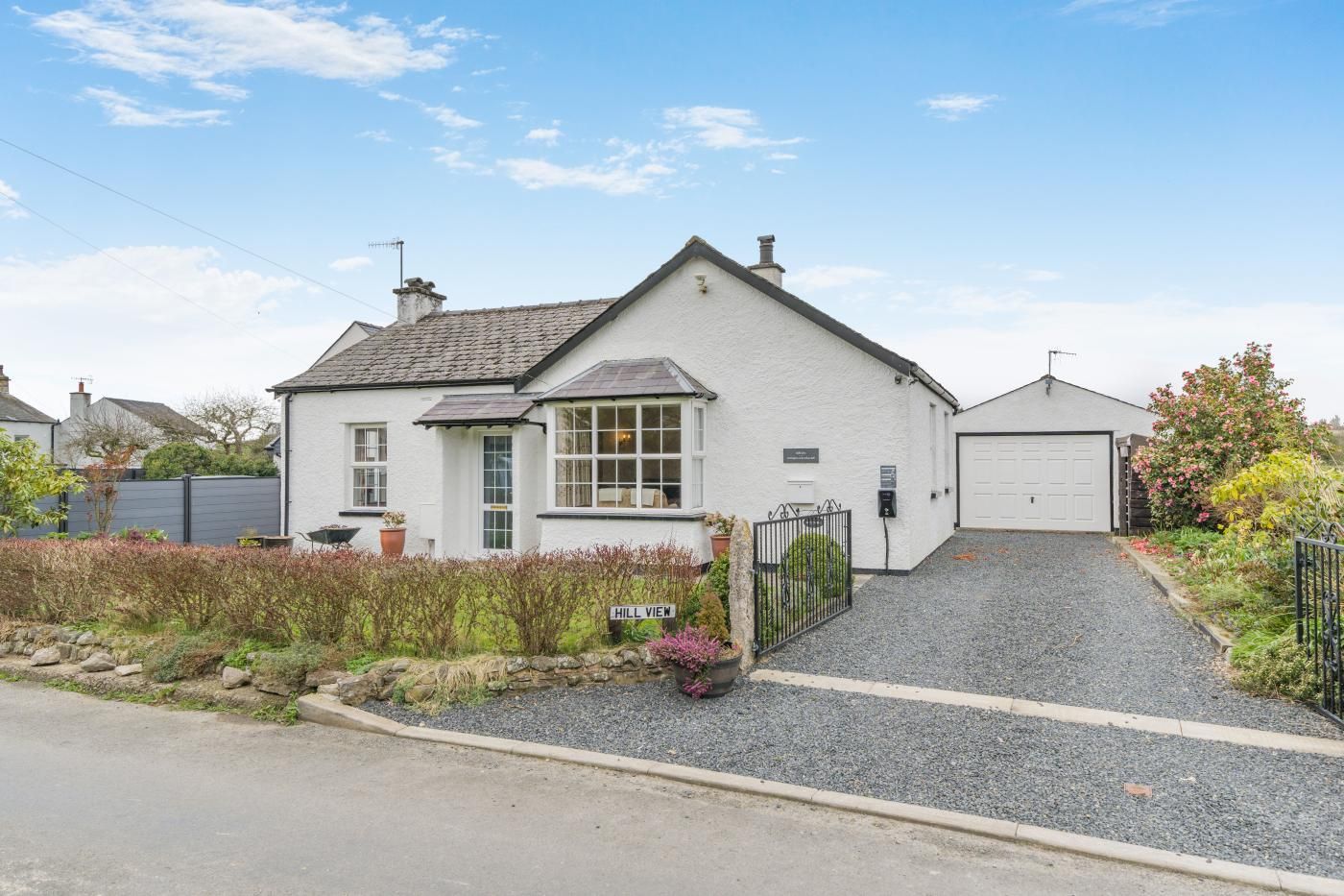 Une maison blanche à deux étages, avec un garage, une allée en gravier et un panneau indiquant « Hill View ».