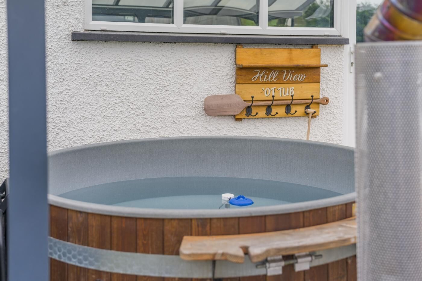 A hot tub with a wooden sign above it, a window, and a metal grill.