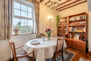 A dining room with a round table, chairs, a chandelier, a bookshelf, and a window with curtains. - 2 Bed in Crooklands (oc-h38250) (Crooklands)