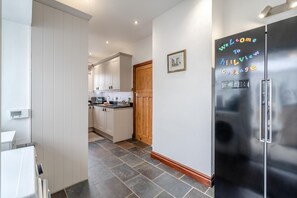 A modern kitchen with white cabinets, a black refrigerator with a welcome sign, and a wooden door. - 2 Bed in Crooklands (oc-h38250) (Crooklands)